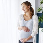 Cheerful pregnant woman looking through window